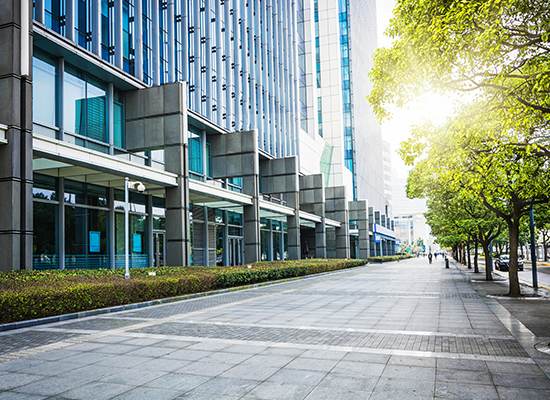 A sidewalk with trees and buildings in the background.